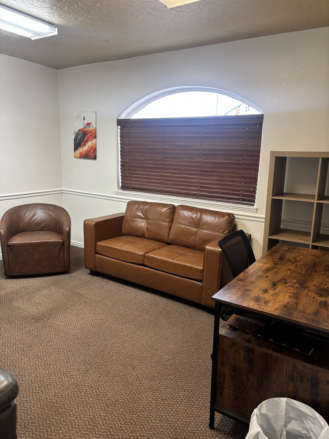 Counseling room with a brown leather sofa and chair beside an arched window