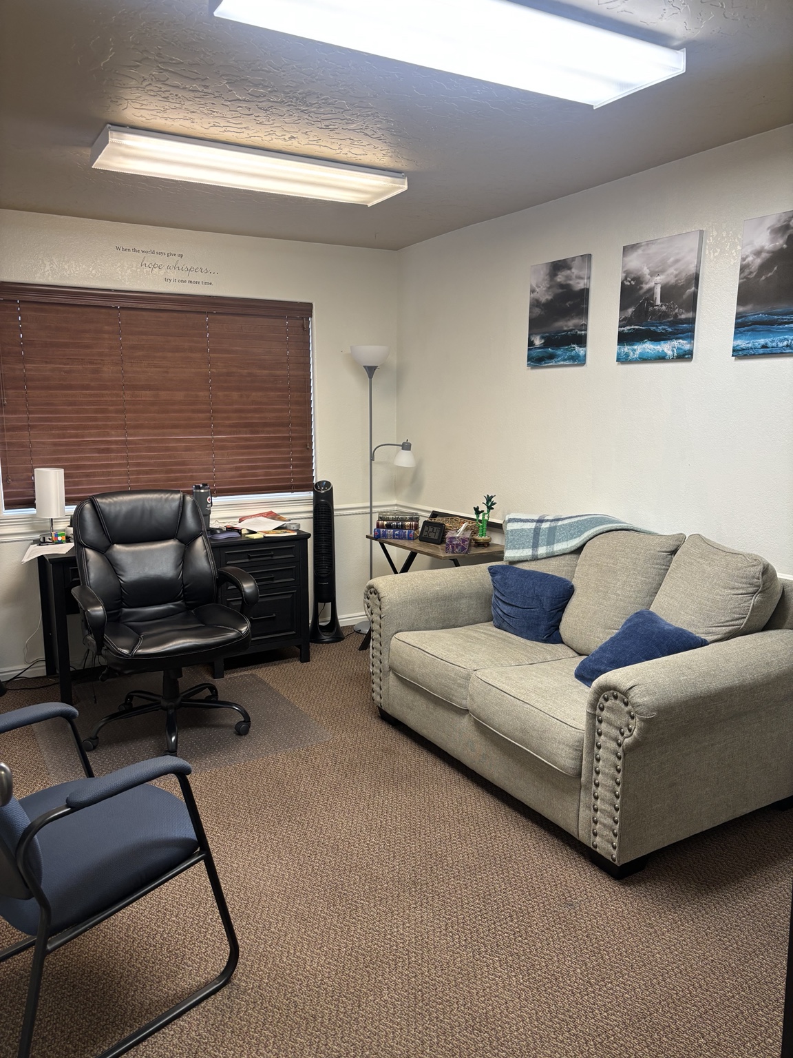 Counseling office with a gray loveseat, blue cushions, and lighthouse artwork